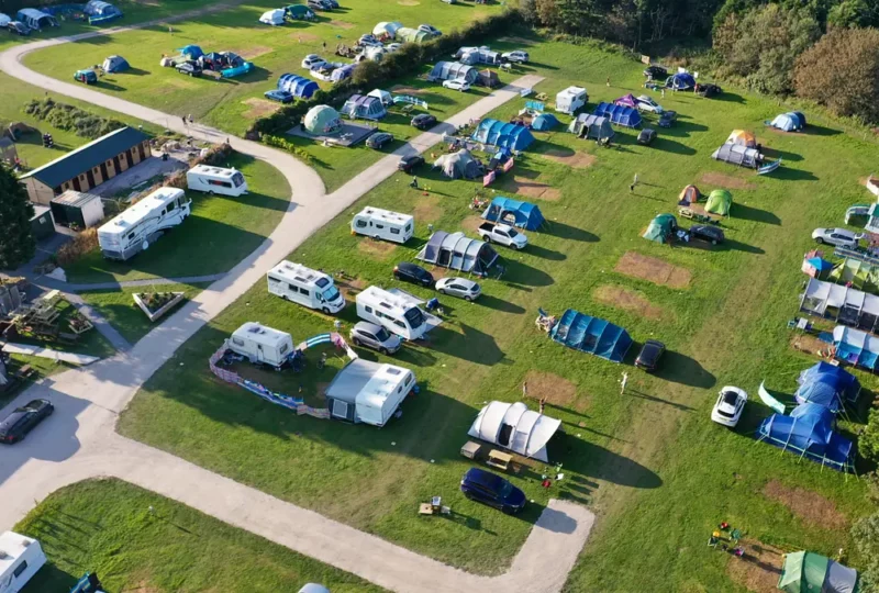Aerial view of a campsite with tents, caravans, and vehicles on a sunny day