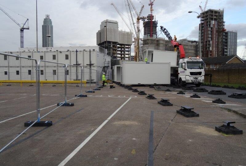 Modular building being installed at a construction site with urban skyline and cranes in the background