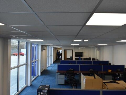 Spacious interior of a modular office with cubicles, blue dividers, and large windows providing natural light