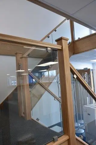 Staircase enclosed with wooden railings and glass panels inside an office building