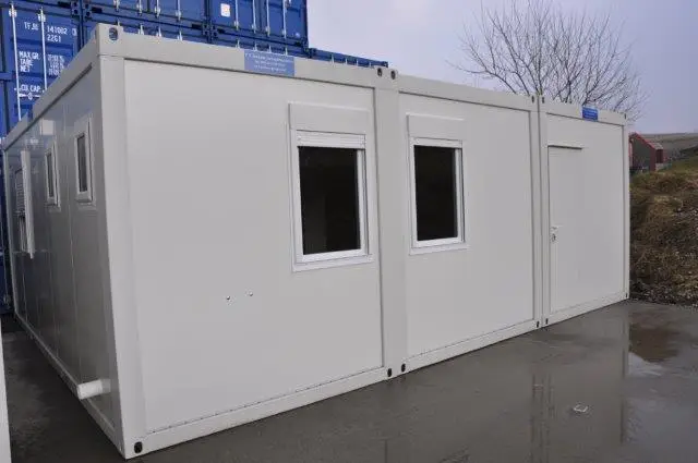Exterior view of a long white modular building with several windows, set on a wet pavement
