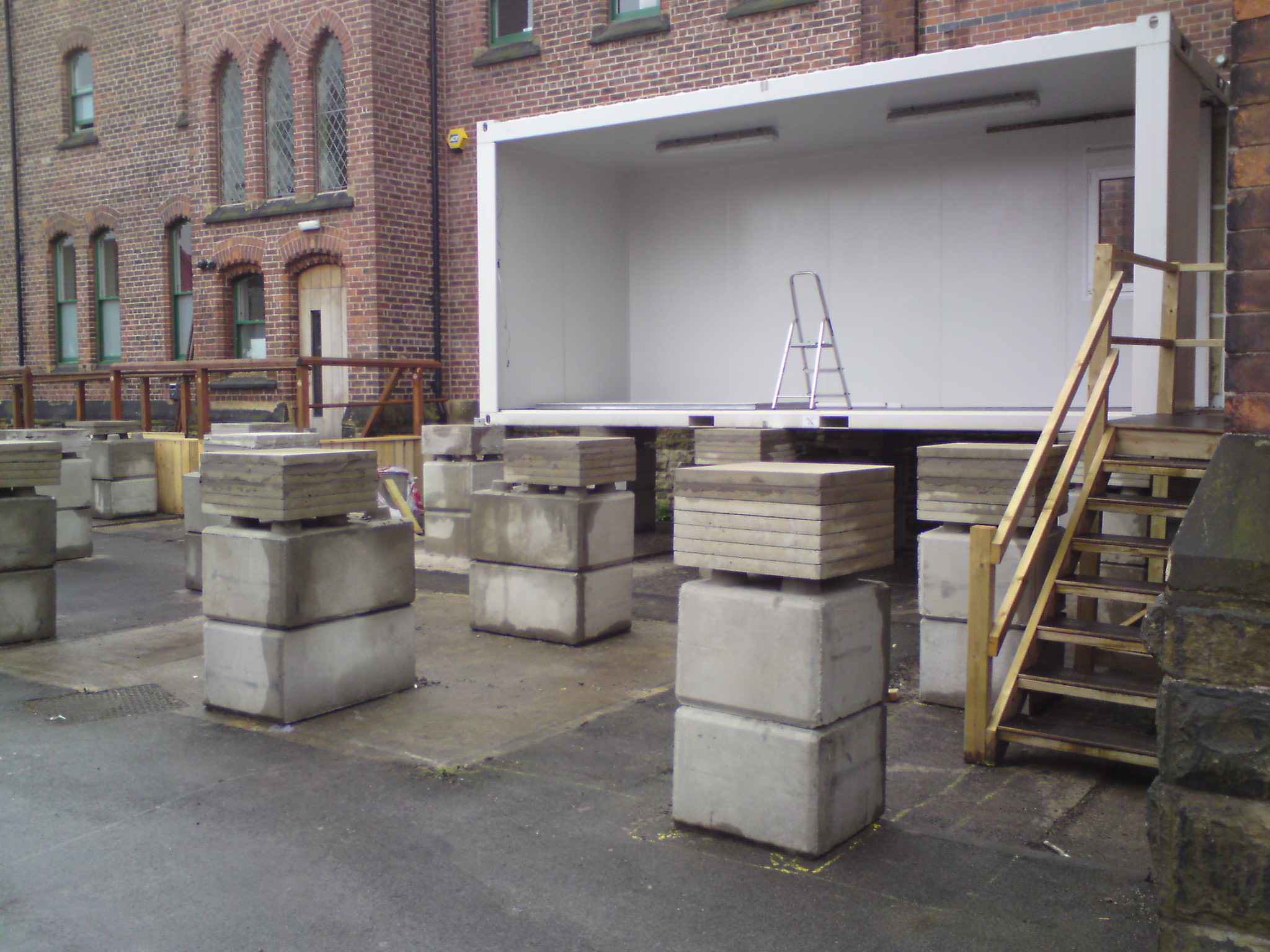 Modular building accessed by wooden stairs, positioned near a historic brick structure