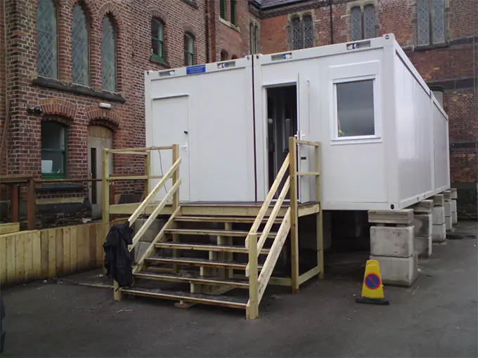 Modular building with a wooden staircase set against a backdrop of a brick building